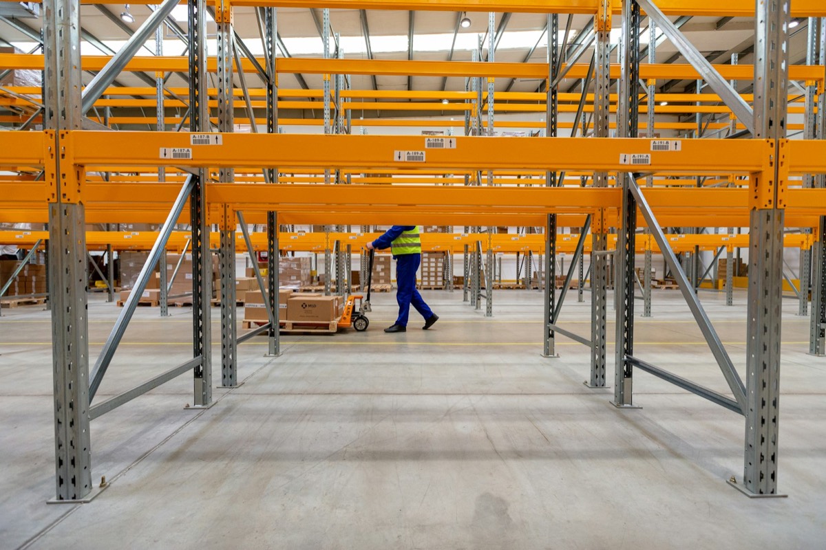 A worker pulls a pallet jack through tall warehouse racking